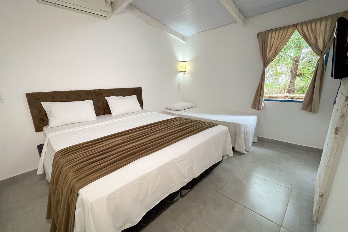 A hotel room with two beds, a wall-mounted air conditioner, a window with curtains, and a wall-mounted light fixture.
