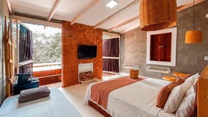 A modern bedroom with a large bed, a TV mounted on a brick wall, and a balcony with curtains. - Ranchos 30 Hotel Fazenda (Hidrolandia)