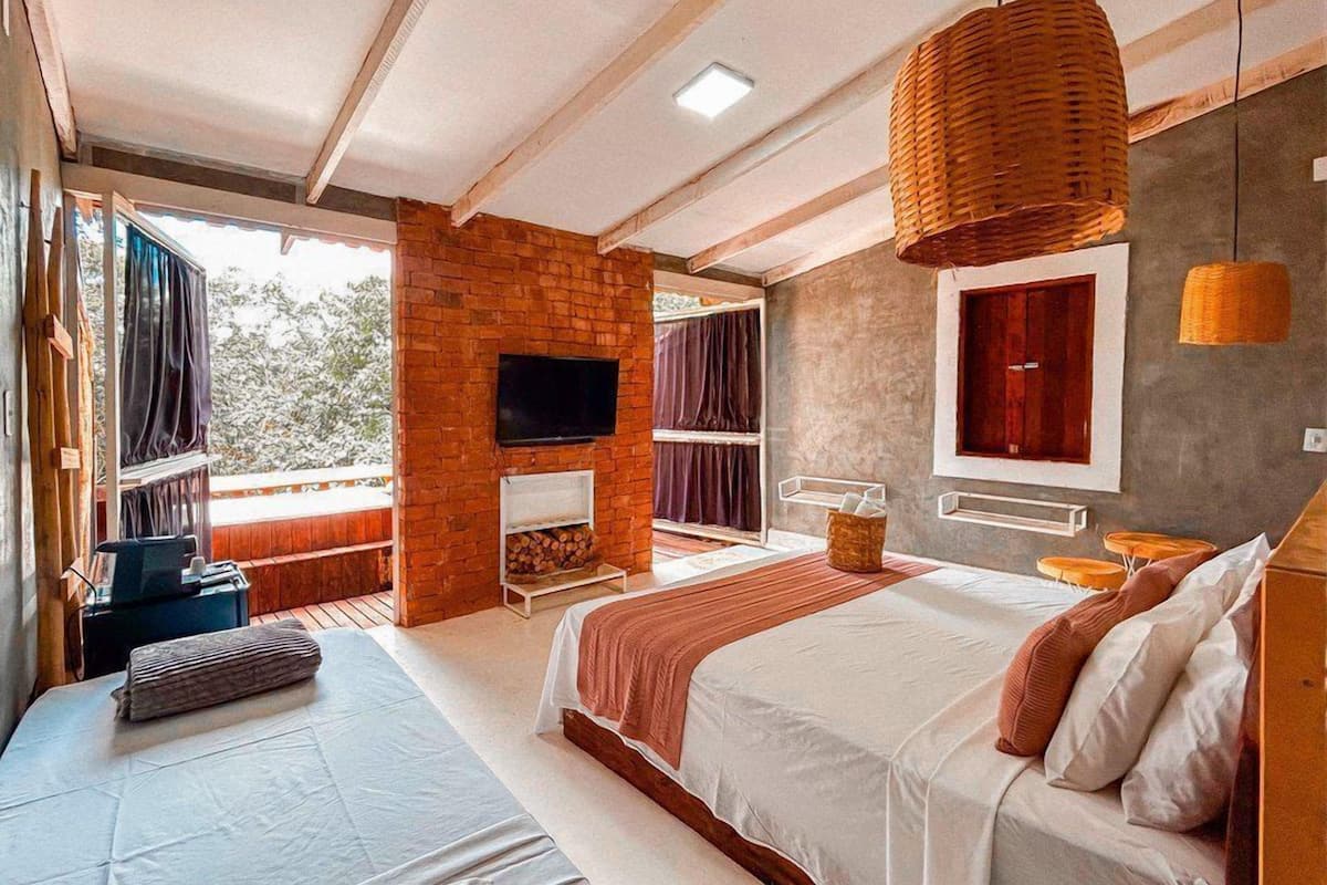 A modern bedroom with a large bed, a TV mounted on a brick wall, and a balcony with curtains.