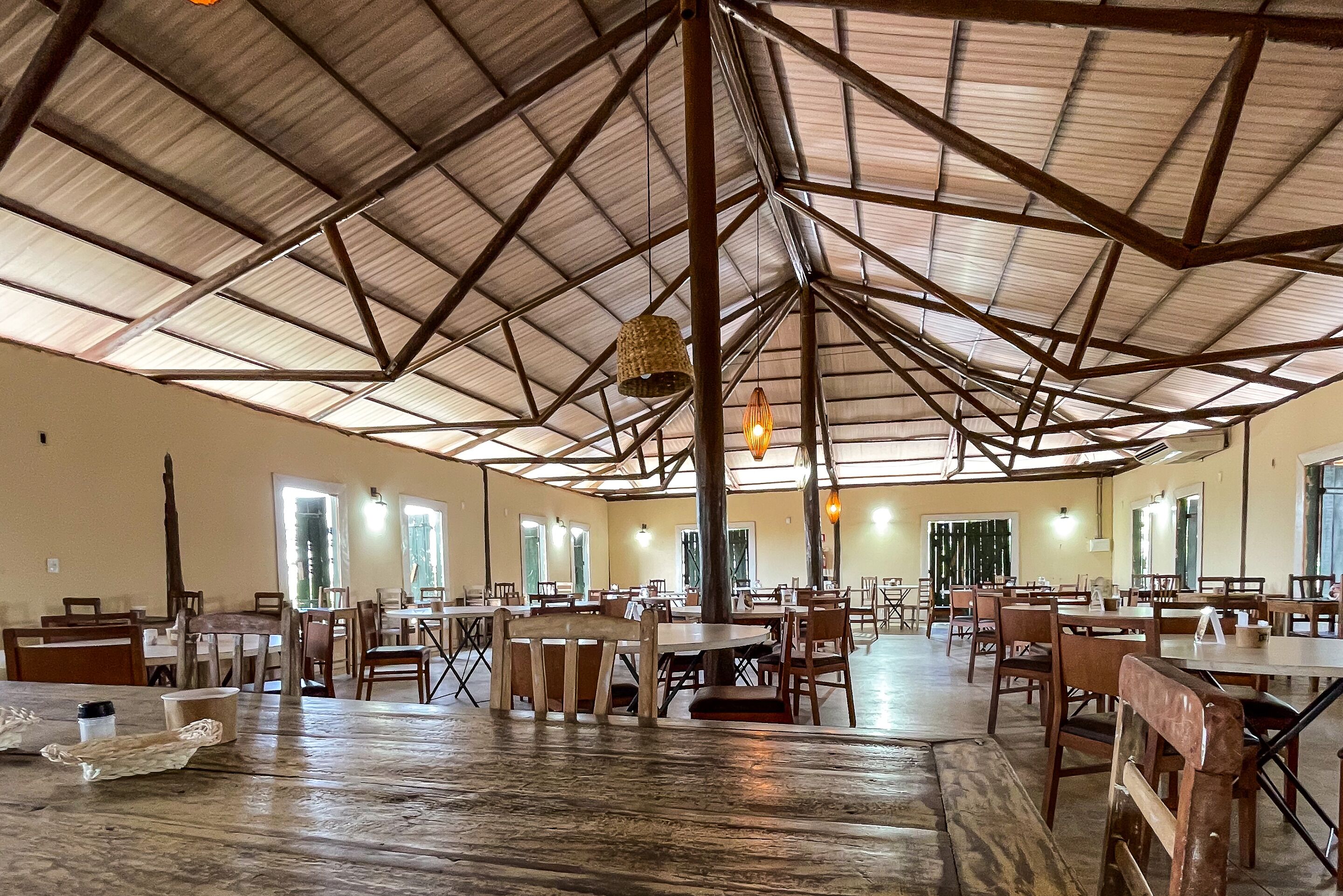 Une salle à manger spacieuse, dotée de hauts plafonds et baignée de lumière naturelle. Des tables et des chaises y sont disposées pour les repas.