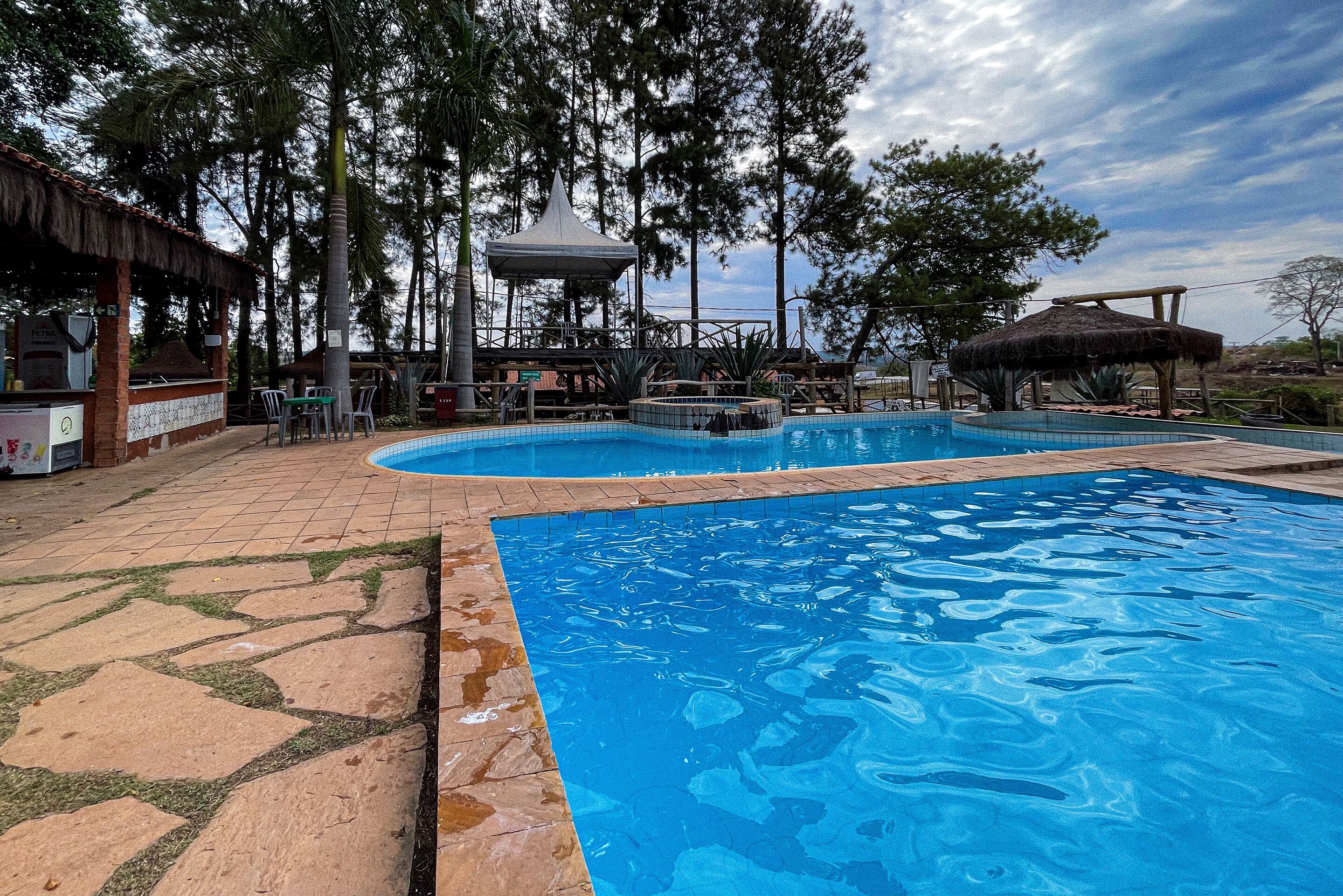 Piscina com deck de pedra e um gazebo ao fundo.