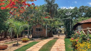 A stone pathway leading to a rustic building with a stone facade, surrounded by lush greenery and flowering plants. - Ranchos 30 Hotel Fazenda (Hidrolandia)