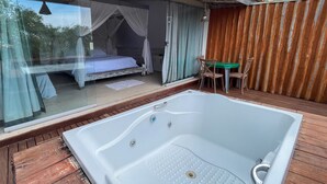 A room with a large bathtub, a bed with a canopy, and a table with chairs. - Ranchos 30 Hotel Fazenda (Hidrolandia)