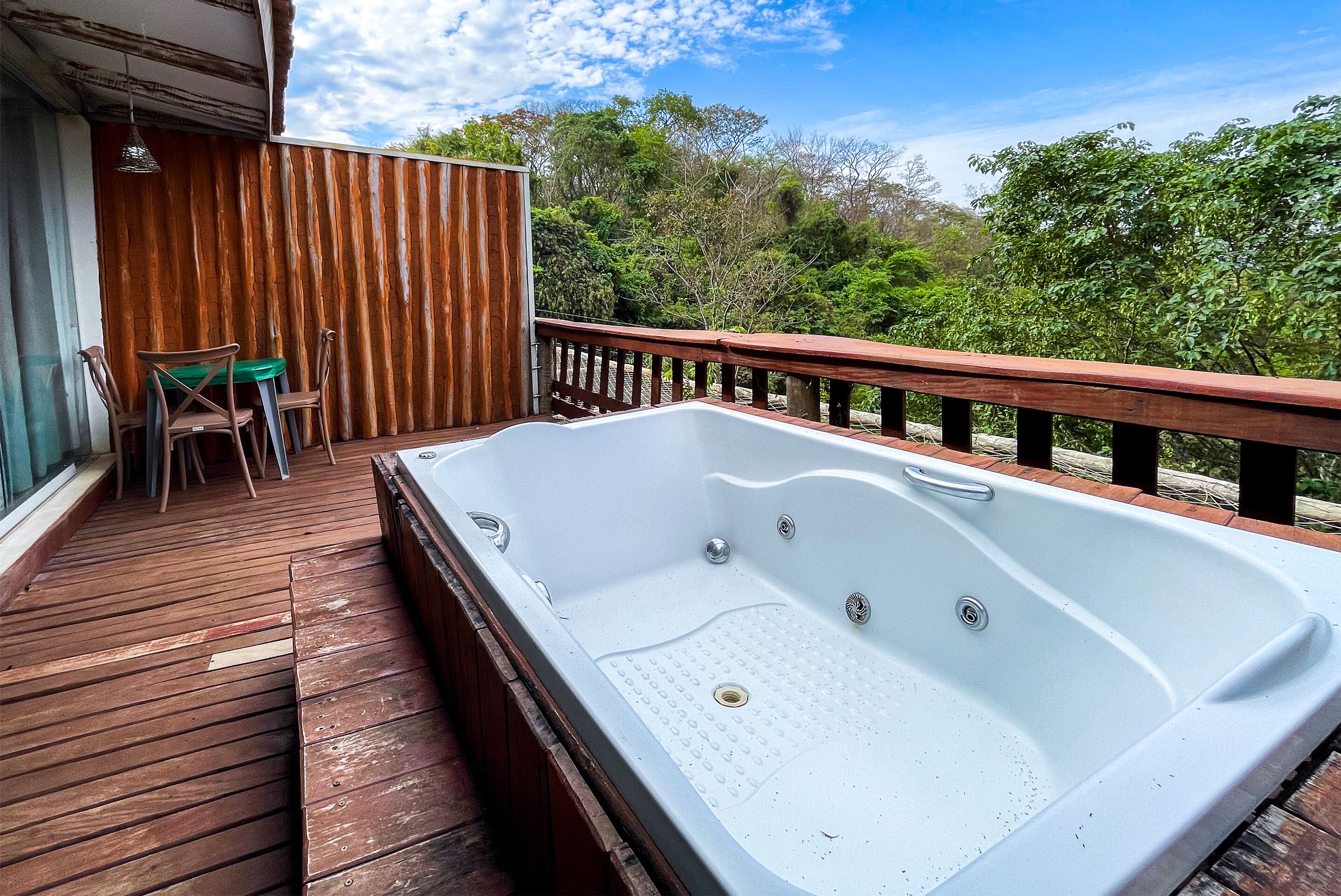 A wooden deck with a hot tub, a table, and chairs.