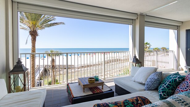 Un balcon avec vue sur la plage, un canapé blanc, une petite table et des coussins décoratifs.