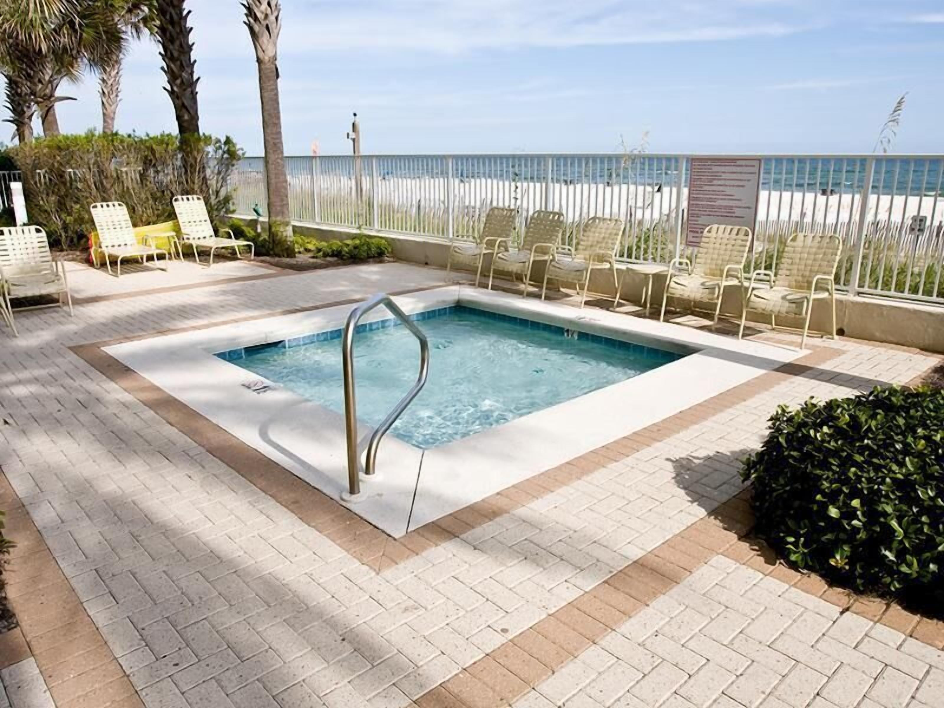 A rectangular pool with a metal ladder, surrounded by white lounge chairs and a white fence.