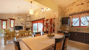A spacious living area with a stone wall, a fireplace, a television, a dining table with chairs, and a bookshelf. - Sea View Nisaki Villa with private pool! (Zakynthos)