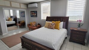 Quarto com uma cama grande, mesa de cabeceira, cômoda, espelho e duas janelas com persianas.