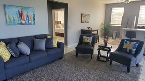 Sala de estar com um sofá azul escuro, duas poltronas, uma mesa de centro e um quadro com barcos à vela.