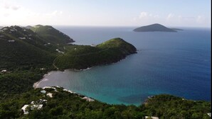 Paisagem costeira com colinas verdejantes, mar azul cristalino e uma pequena ilha ao longe.