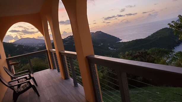 Varanda com vista para uma paisagem montanhosa e um corpo de água ao pôr do sol.