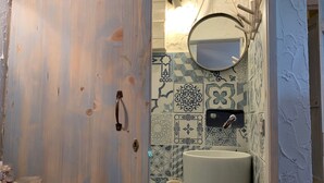 A bathroom with a wooden door, a white sink, and patterned tiles. - Casetta Ale 20 mt from the sea (Tancau Sul Mare)