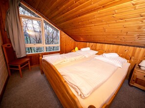A wooden-paneled room with a large bed, a chair, a nightstand, and a window with curtains. - Haus am Wald by Interhome (Extertal)