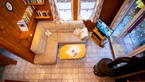 Una sala de estar acogedora con un sofá modular, una mesa de centro de madera y un televisor. Se observa una estantería llena de libros y un reloj en la pared.