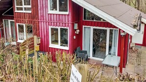 Una casa de madera roja con varias ventanas, una chimenea y un patio con mobiliario exterior.