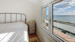 A bedroom with a bed, a nightstand, a lamp, and a view of the sea through a large window. - La Grande Côte by Interhome (Saint Palais sur mer)