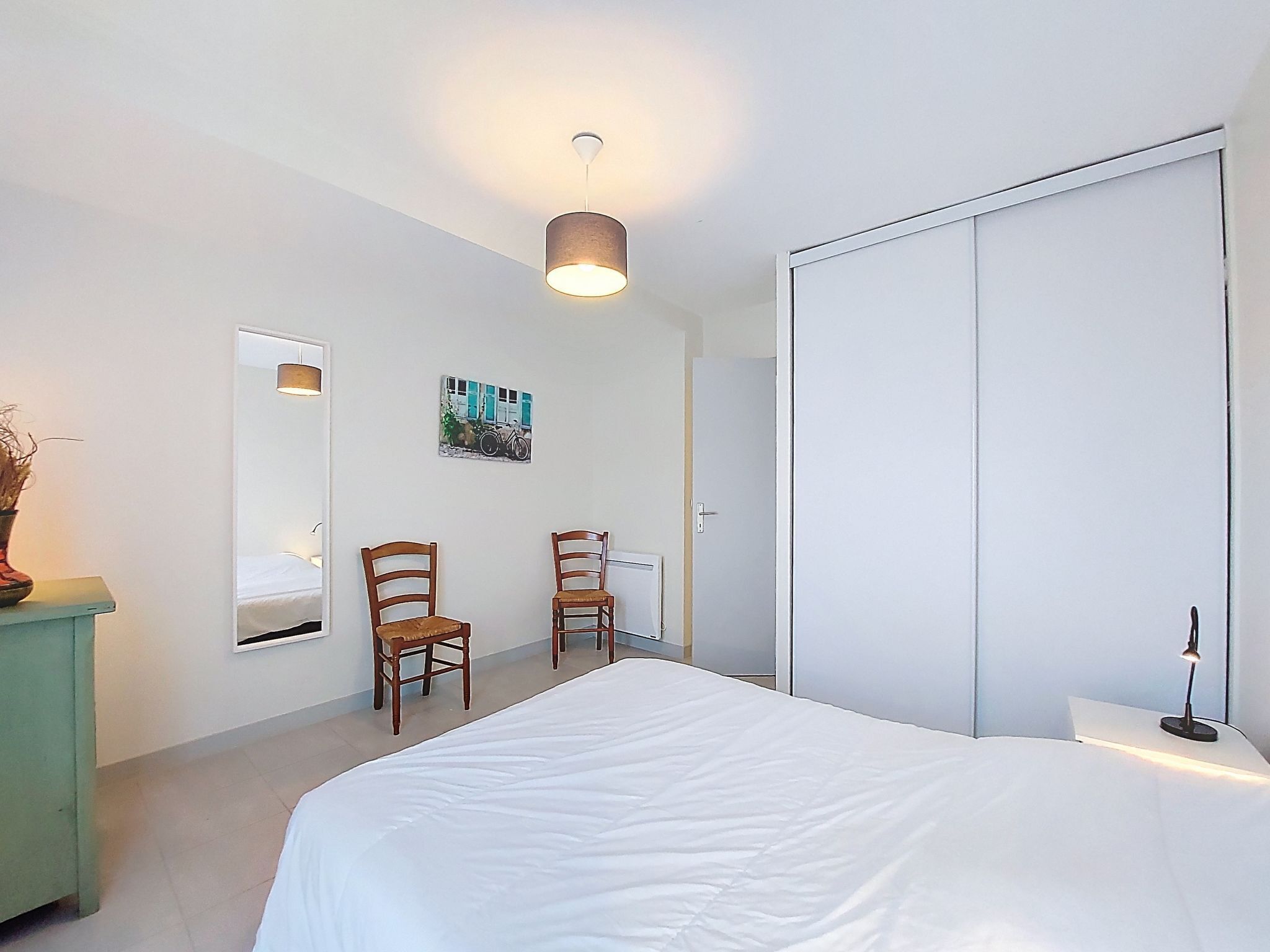 Une chambre à coucher comprenant un lit, deux chaises, une commode, un tableau et une armoire.