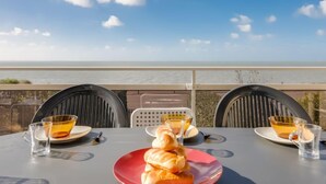 A table with a croissant, two glasses of tea, and a red plate, overlooking a beach with a clear sky. - La Grande Côte by Interhome (Saint Palais sur mer)