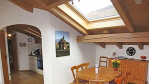 A dining area with a wooden table and chairs, a clock on the wall, and a skylight above. - Wohnung 8 (Am Sonneneck) by Interhome (Ruhpolding)