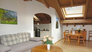A living room with a sofa, a wooden coffee table with flowers, a dining area with a table and chairs, and a kitchen in the background. - Wohnung 8 (Am Sonneneck) by Interhome (Ruhpolding)