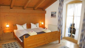 A wooden-framed bedroom with a bed, two bedside lamps, a radiator, and a window with curtains. - Wohnung 8 (Am Sonneneck) by Interhome (Ruhpolding)