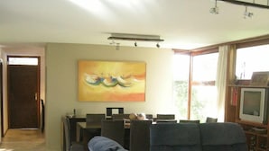 Un salón con un sofá, una mesita de centro y una televisión. Hay un cuadro en la pared y una puerta que da a otra habitación.