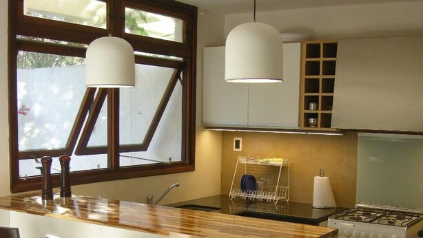 Una cocina con una isla central, taburetes de bar, estufa y lámparas colgantes.