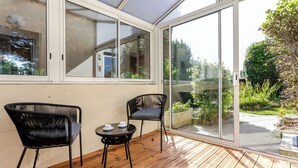 A sunlit room with a wooden floor, two black chairs, a small table, and a large sliding glass door leading to an outdoor garden. - Le Petit Robinson by Interhome (Dinard)