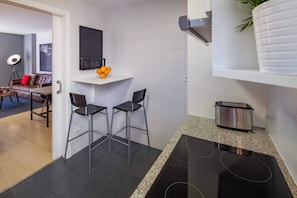 Une cuisine compacte dotée d’une cuisinière intégrée, d’un petit plan de travail et de deux tabourets de bar.