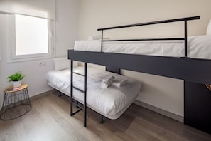 A bunk bed room with a window, a small stool with a plant, and a wooden floor.