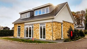 Ein modernes, zweistöckiges Haus mit Steinverkleidung, großen Fenstern und einem geneigten Dach.
