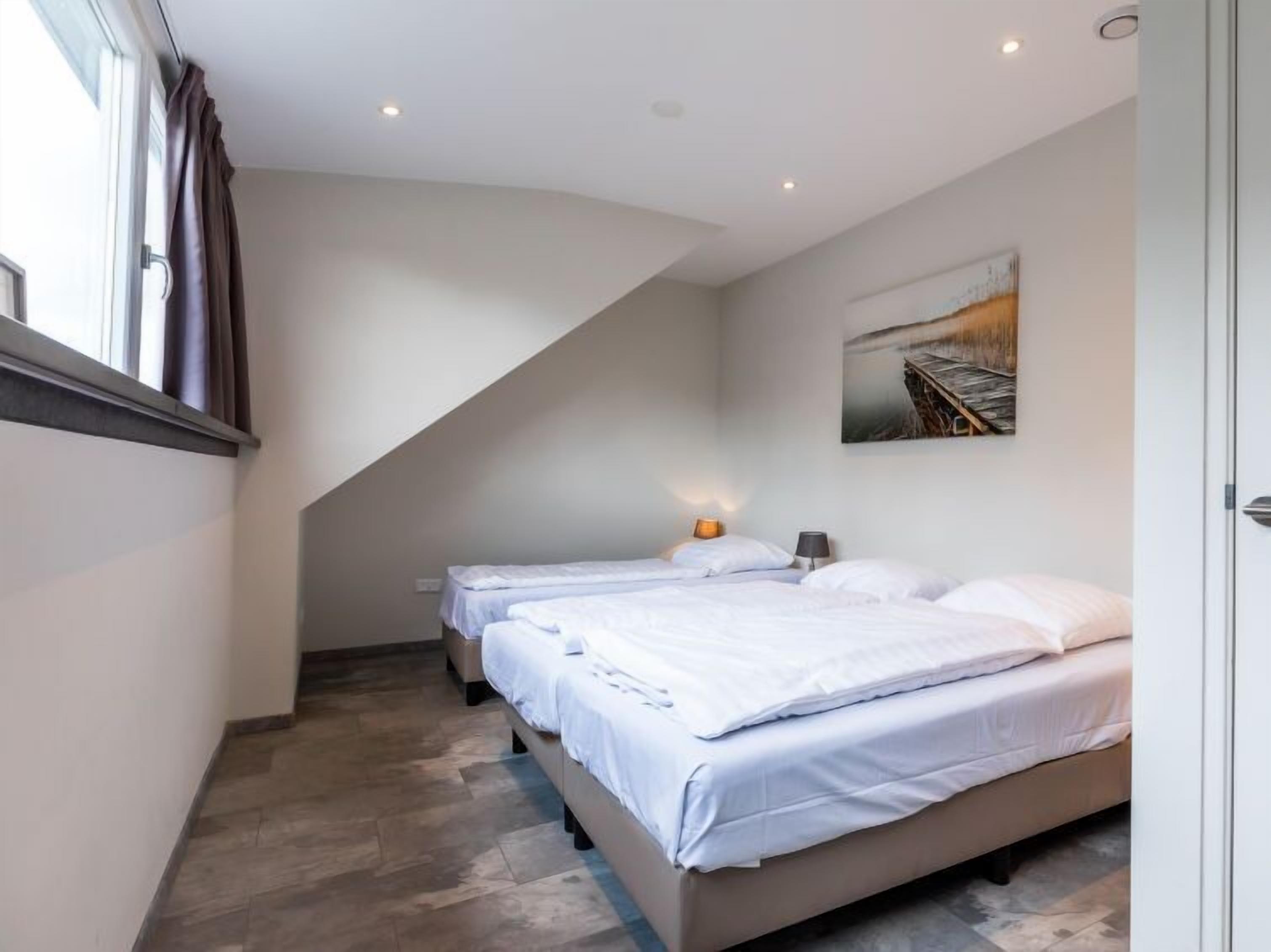 Une chambre d’hôtel moderne avec deux lits, un plafond en pente et un tableau au mur.