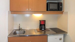 Een kleine keuken met een roestvrijstalen spoelbak, een koffiezetapparaat, een magnetron en een minibar.