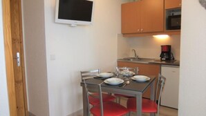 Een praktische keuken met een eettafel voor vier personen, een magnetron, een koffiezetapparaat en een televisie aan de muur.