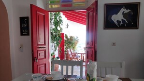 Comedor con mesa dispuesta para dos, que incluye una tetera, tazas y platos. Se observan puertas rojas y un cuadro con caballos.