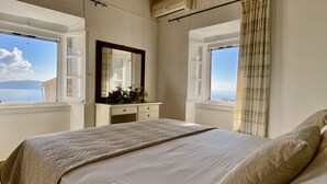 Un dormitorio con cama, cómoda, espejo y dos ventanas con vistas al mar.