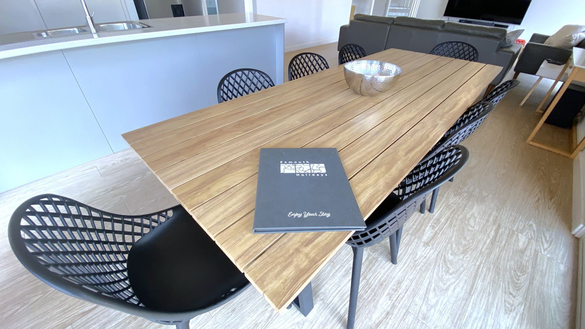 Un espace repas moderne avec une table en bois, des chaises noires et une brochure intitulée « Vacances à Exmouth ».