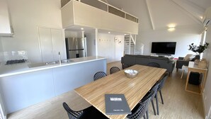 Eine moderne Küche mit Kochinsel, ein Essbereich mit Holztisch und Stühlen sowie ein Wohnbereich mit Sofa und Fernseher.