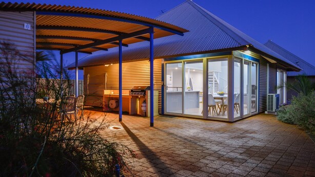 Ein modernes Haus mit überdachter Terrasse, Grillplatz und einem wintergartenartigen Essbereich.