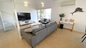 Ein modernes Wohnzimmer mit grauem Sofa, einem Flachbildfernseher, einem Couchtisch und einem Essbereich mit weißem Tisch und Stühlen.