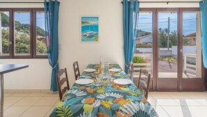 Un coin repas avec une table dressée pour quatre personnes, des rideaux bleus et une vue sur la campagne.