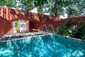 Una piscina con borde de azulejos, rodeada de follaje y una estructura de madera.