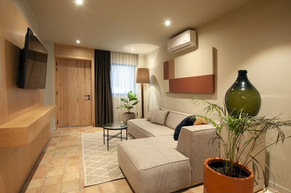 Una sala moderna con un sofá, una mesa de centro, una planta en maceta y un televisor de pantalla plana montado en la pared.