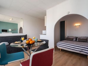 A modern living room with a glass dining table, a sofa, and a bed with striped bedding.