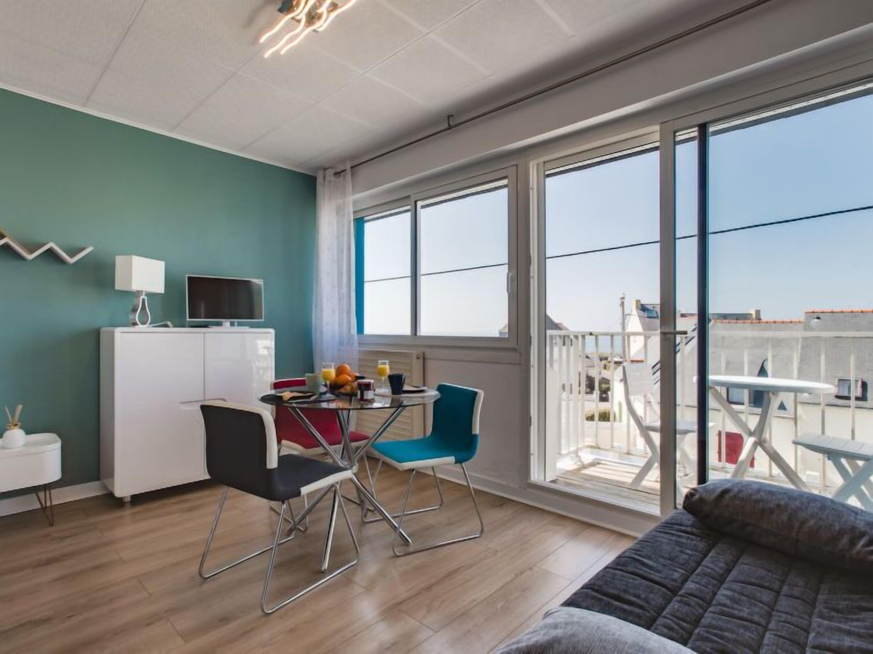 A modern room with a dining area, a sofa, and a balcony with a view.