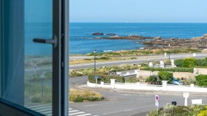 A coastal view from inside a building, featuring a road with a roundabout, a pedestrian crossing, and a rocky shoreline with the ocean in the background. - Les Brisants by Interhome (Quiberon)