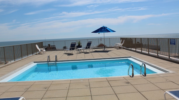 A pool area with a view of the ocean, a blue umbrella, and lounge chairs. - Steps to Boardwalk & Ocean! (Rehoboth Beach)