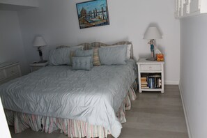 Un dormitorio con una cama grande, una mesita de noche con lámpara, una pequeña mesa con lámpara y una estantería.