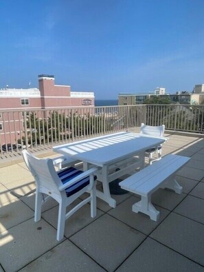 Un patio exterior blanco con una mesa y bancos, con vistas a una zona residencial y al mar.