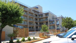 A multi-story residential building with balconies, a gated entrance, and a parking area with cars. - Fantastic Views of Ocean from the Extra-large Patio! (Rehoboth Beach)